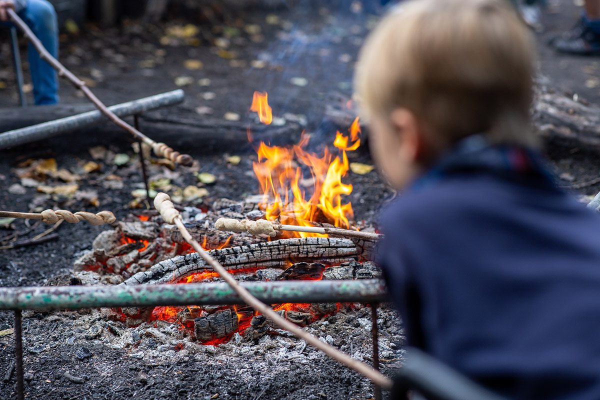 ein Kind sitzt vor einem Lagefeuer und hält ein Stockbrot in die Flammen